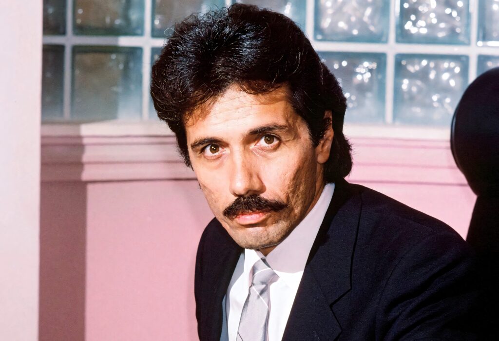 Edward James Olmos portrait in sharp suit with mustache against pink glass block background Wallpaper