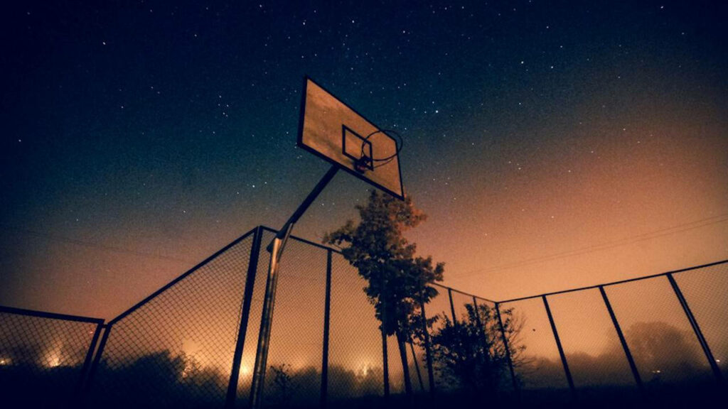 Dusk's Embrace: Capturing the Coolness of a Basketball Court Enclosed by a Fence, with an Empty Ring Standing Tall Wallpaper
