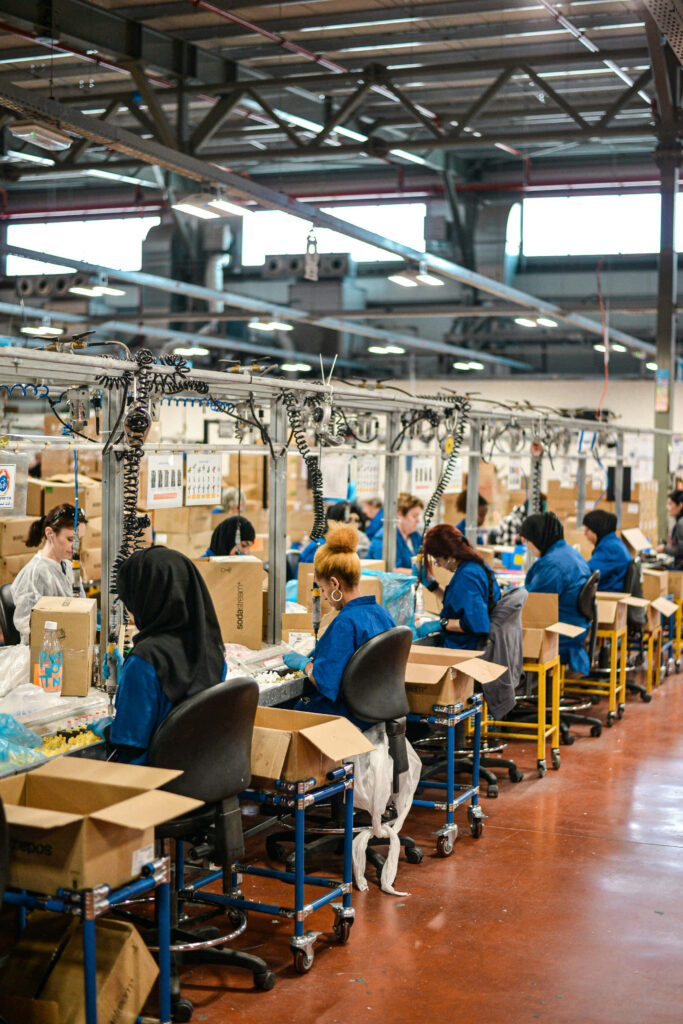 Busy factory production line with workers in blue uniforms assembling products efficiently Wallpaper