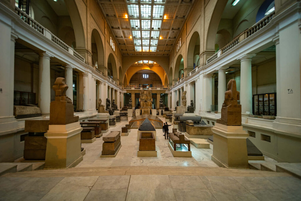 Egyptian Museum interior with arched ceilings columns ancient statues sarcophagi warm tones wallpaper
