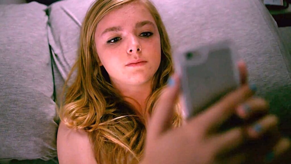 Elsie Fisher as Kayla Day lying on bed with phone soft lighting authentic Eighth Grade scene Wallpaper
