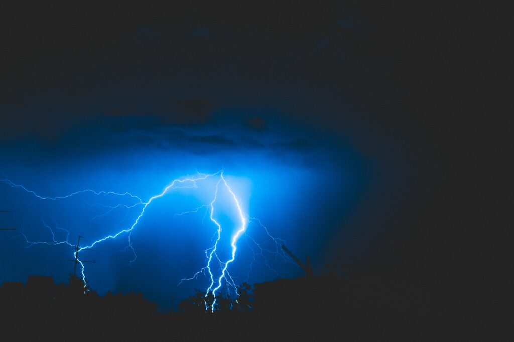Vivid electric blue lightning bolt striking through dark stormy cloudy sky dramatic wallpaper background