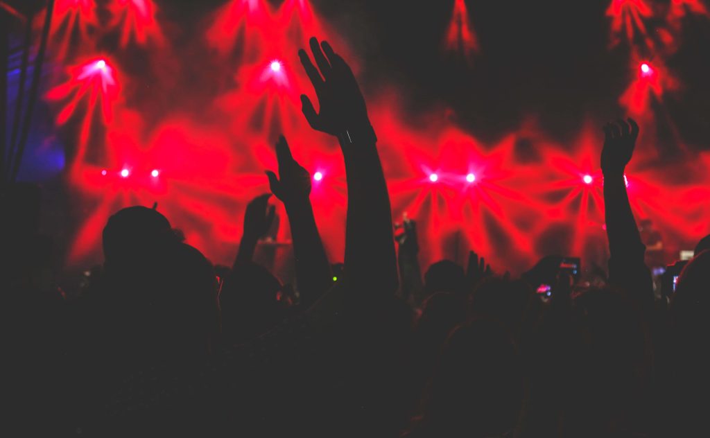 Energetic concert crowd silhouettes cheering under vibrant red stage lights live music wallpaper