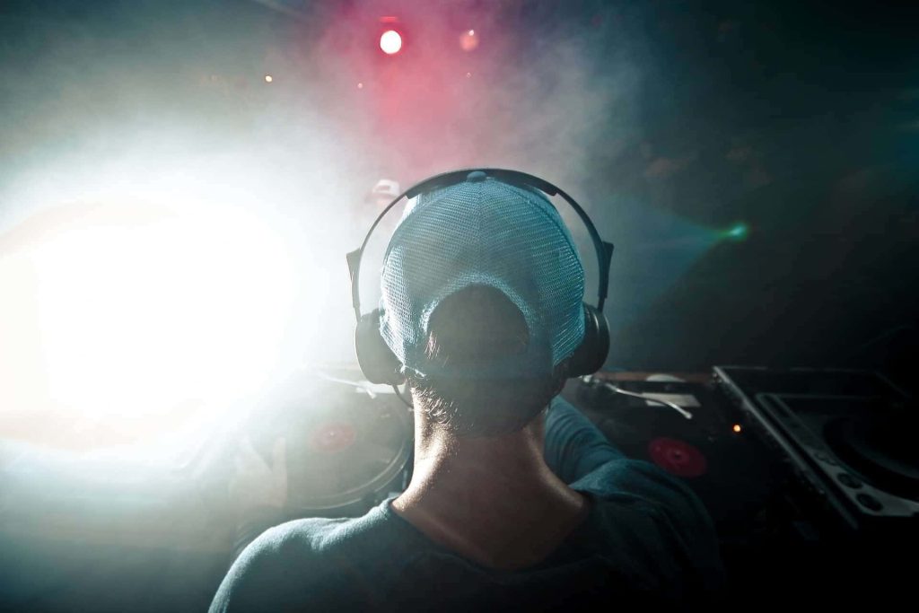 DJ wearing headphones and blue cap mixing on turntables with vibrant stage lighting concert wallpaper