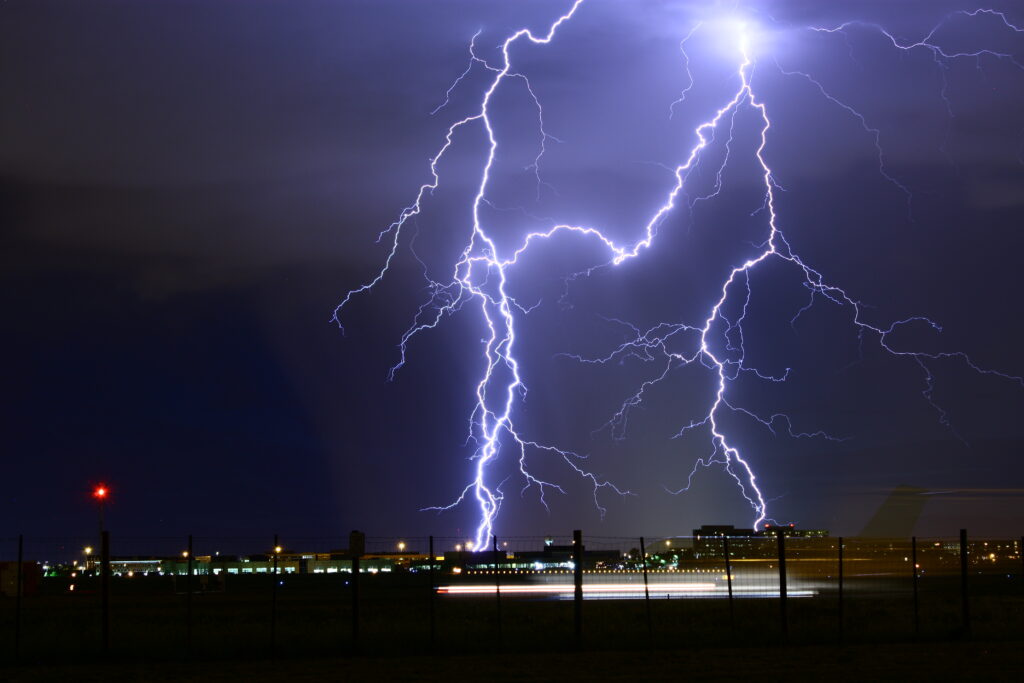 Dramatic lightning bolts illuminate a cloudy night sky above a vibrant city skyline with urban lights Wallpaper