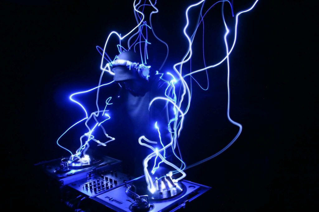 Electric Excitement: A DJ Rocking the Crowd with Cool Beats, Electric Blue Lights on a Black Musical Canvas Wallpaper
