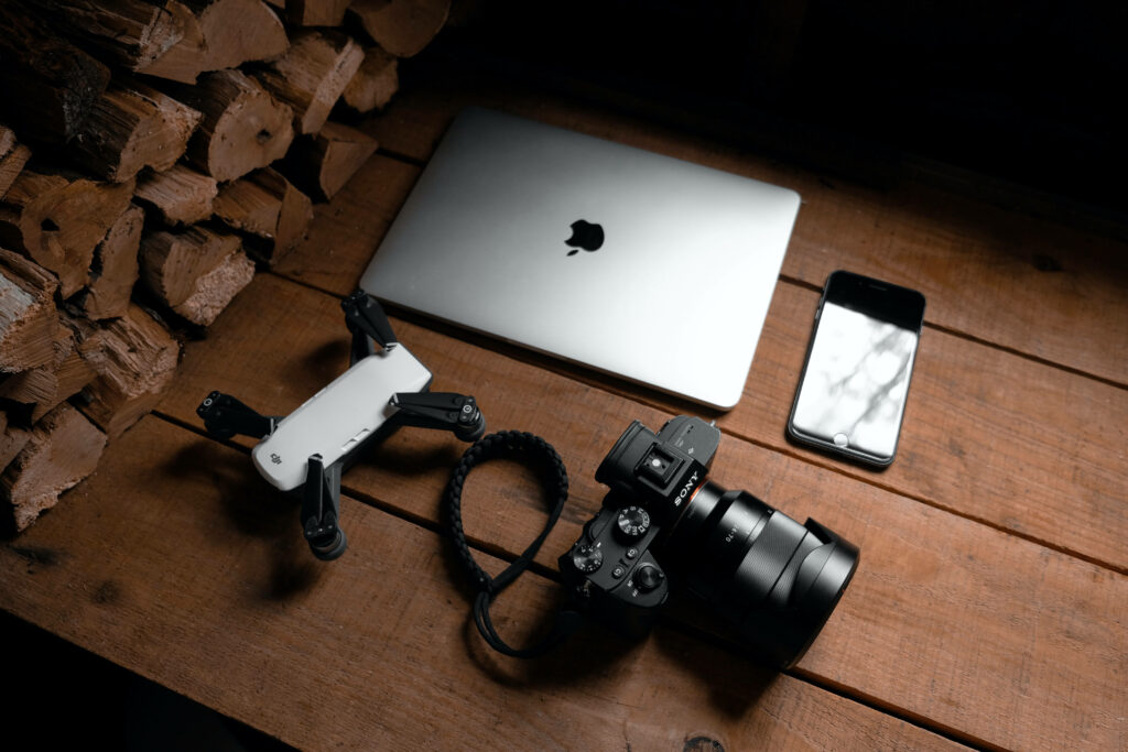 Electronics Setup: DSLR, Laptop, Smartphone & Drone on Rustic Wood Wallpaper