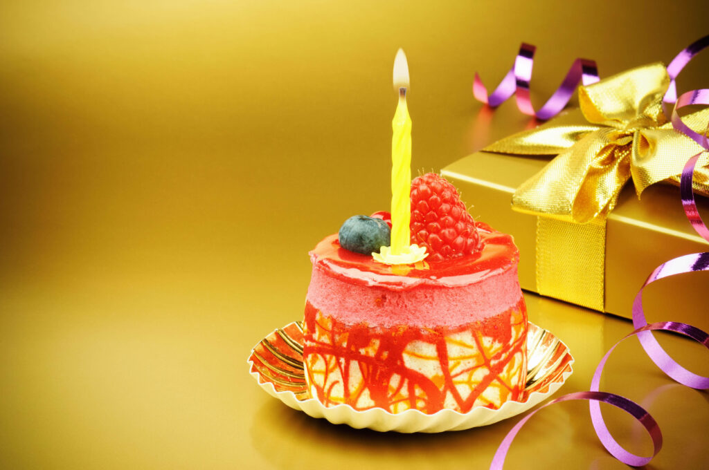 Elegant birthday cake with raspberries blueberries lit candle gold background festive wallpaper
