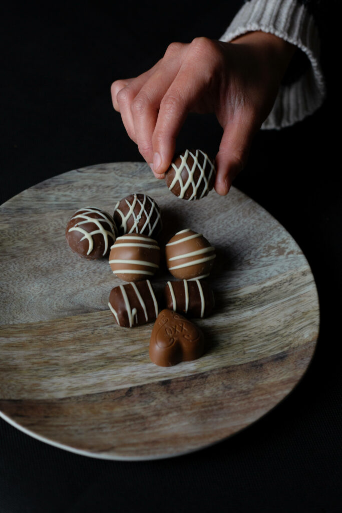 Close-up of assorted chocolate truffles with white drizzle on wooden plate hand reaching dark background Wallpaper