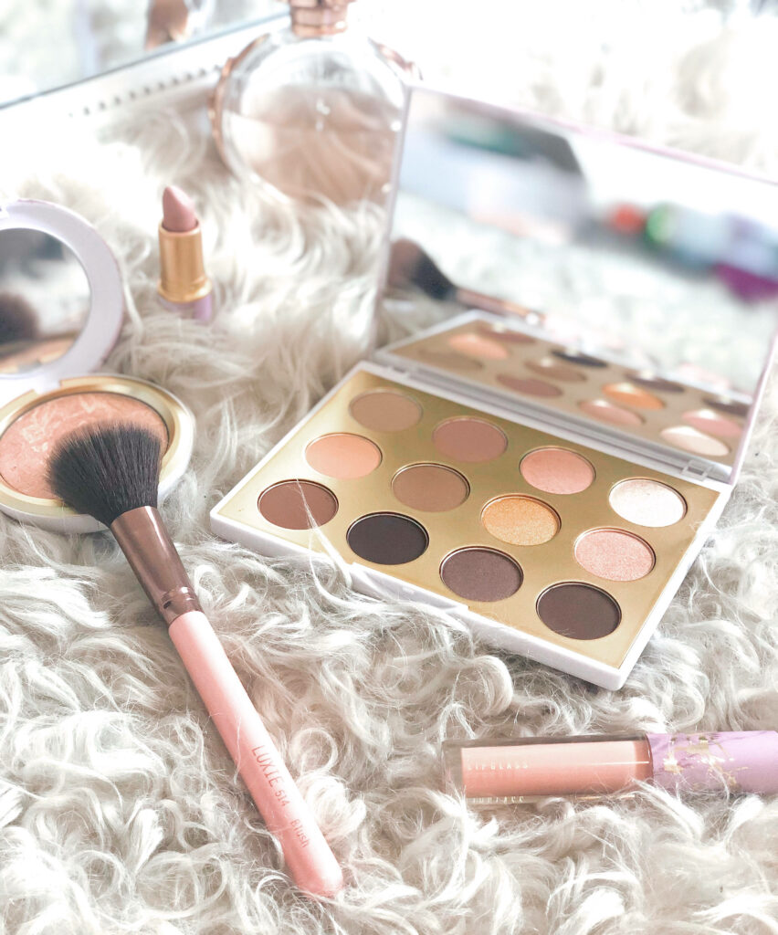 Makeup essentials flat lay with neutral eyeshadow blush brush lipstick on white fur background Wallpaper