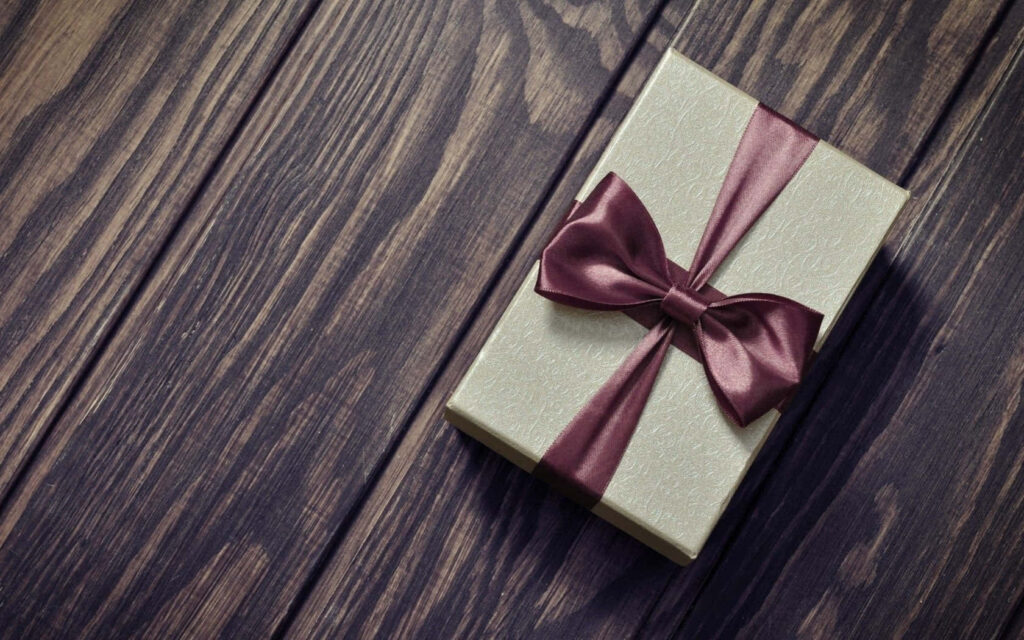 Elegant cream gift box with maroon ribbon on dark wood surface holiday present wallpaper