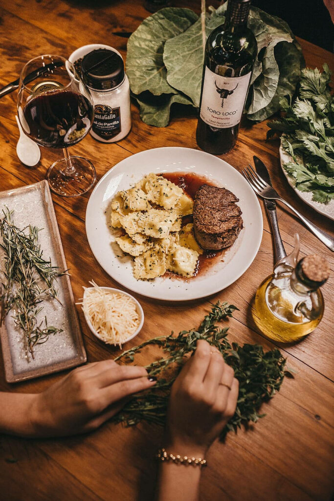 Elegant Dinner Setup with Steak, Ravioli, Wine & Fresh Herbs - Wallpaper