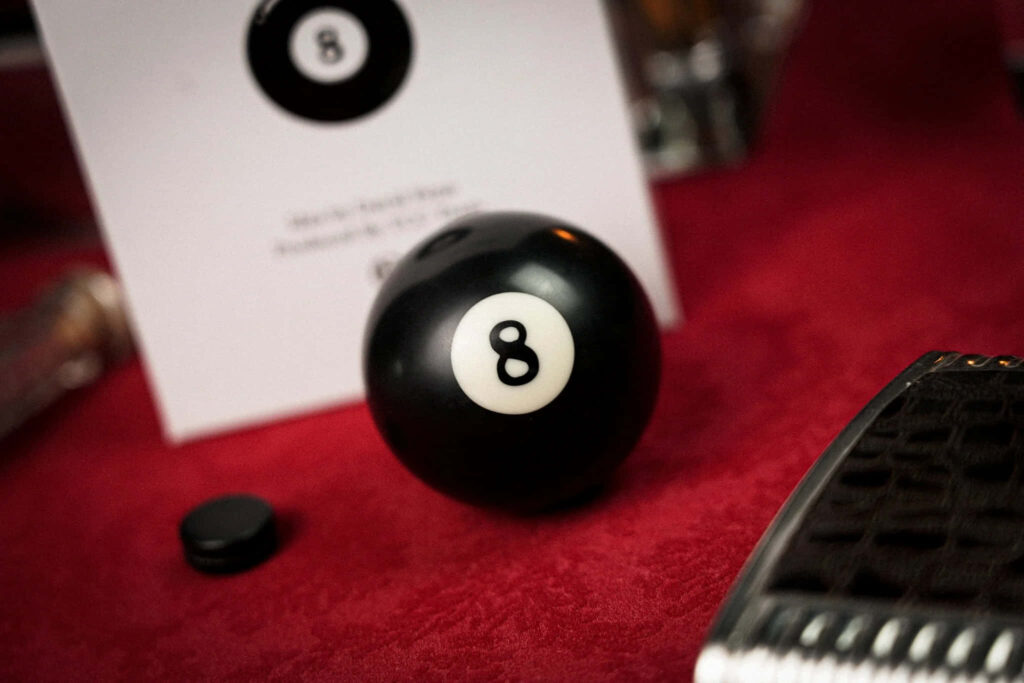 Glossy black eight ball on red felt surrounded by cards elegant classic billiards wallpaper background