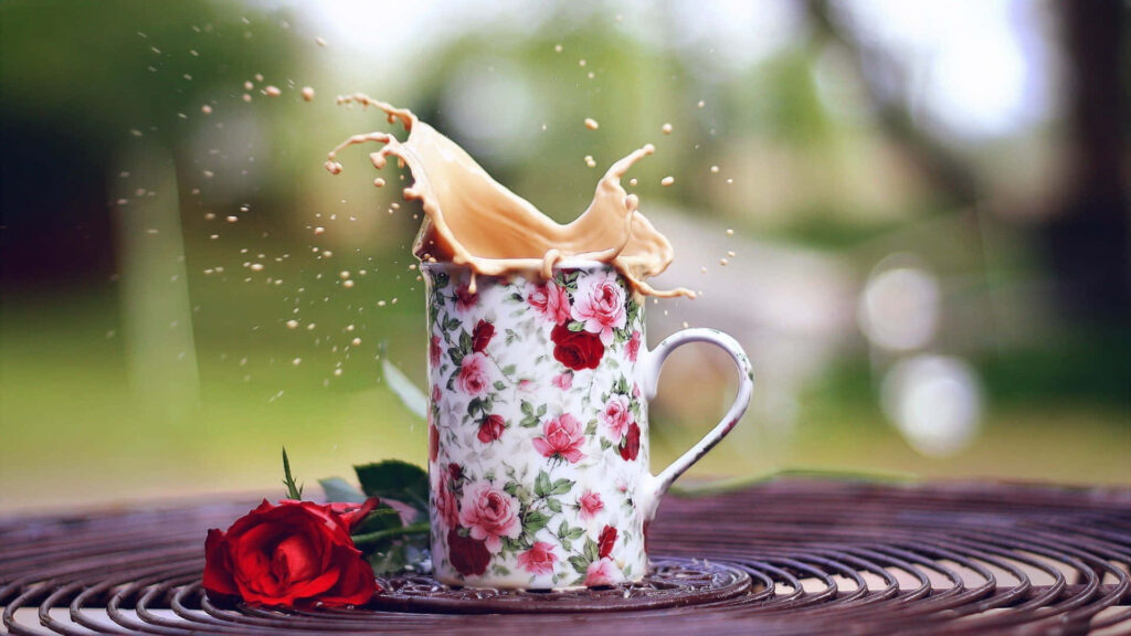 Floral coffee cup with coffee splash and red roses on blurred green background wallpaper