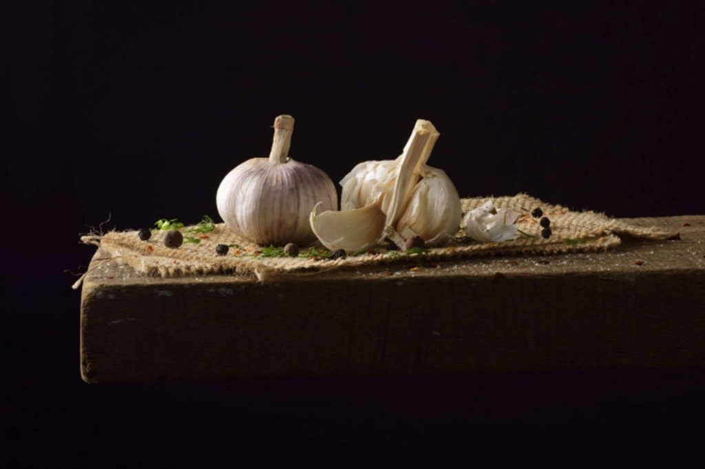 Fresh garlic bulbs and cloves on rustic burlap with peppercorns and herbs on black background Wallpaper
