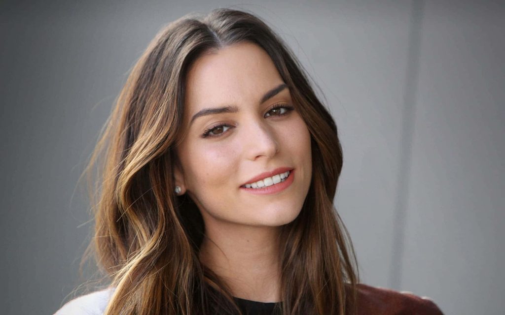 Portrait of Genesis Rodriguez smiling with wavy brown hair and natural lighting on neutral background Wallpaper
