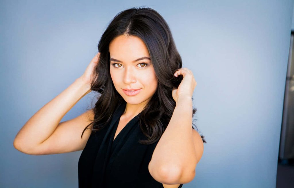 Genevieve Kang portrait with long dark wavy hair in black top against light blue background studio lighting Wallpaper