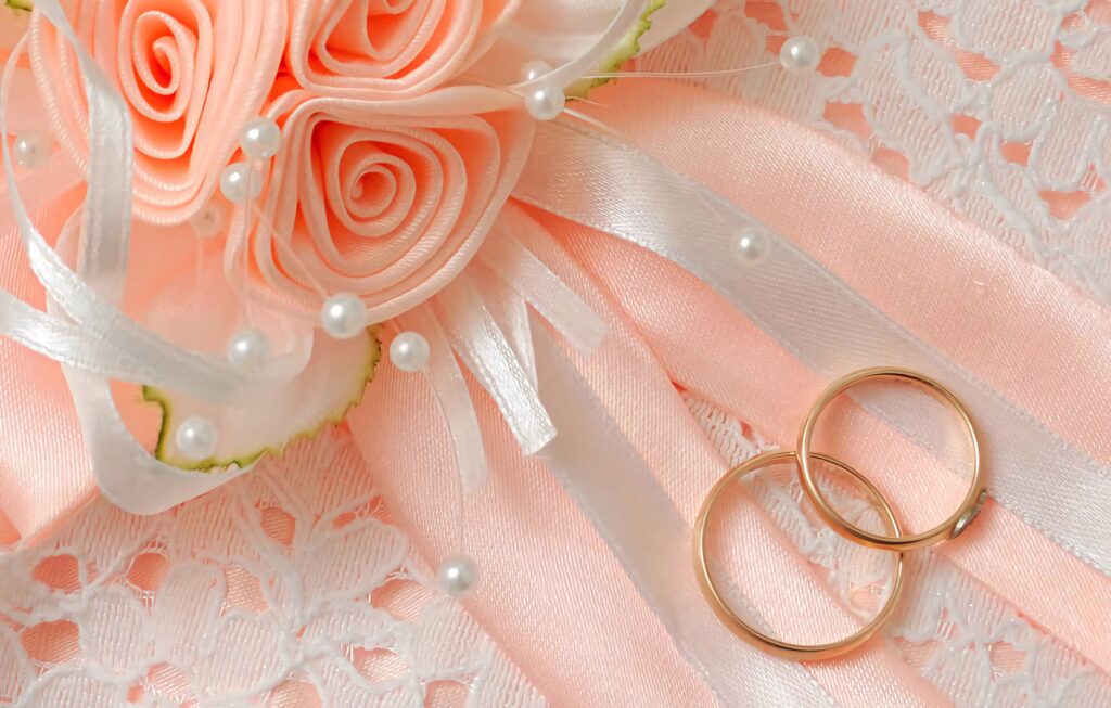 Elegant gold band engagement rings on peach white satin ribbons with pearls and roses background Wallpaper