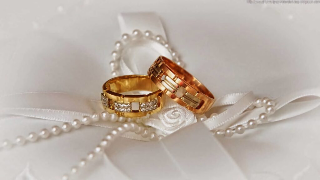 Elegant gold engagement rings with diamonds on white satin ribbon and pearl necklace background Wallpaper
