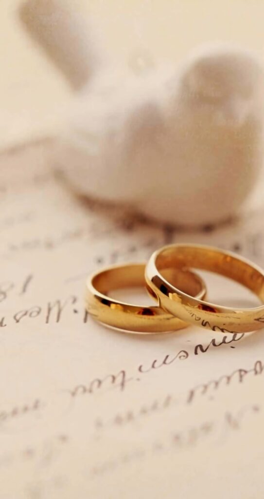 Elegant gold engagement rings on handwritten letters with white bird ornament and creamy background Wallpaper