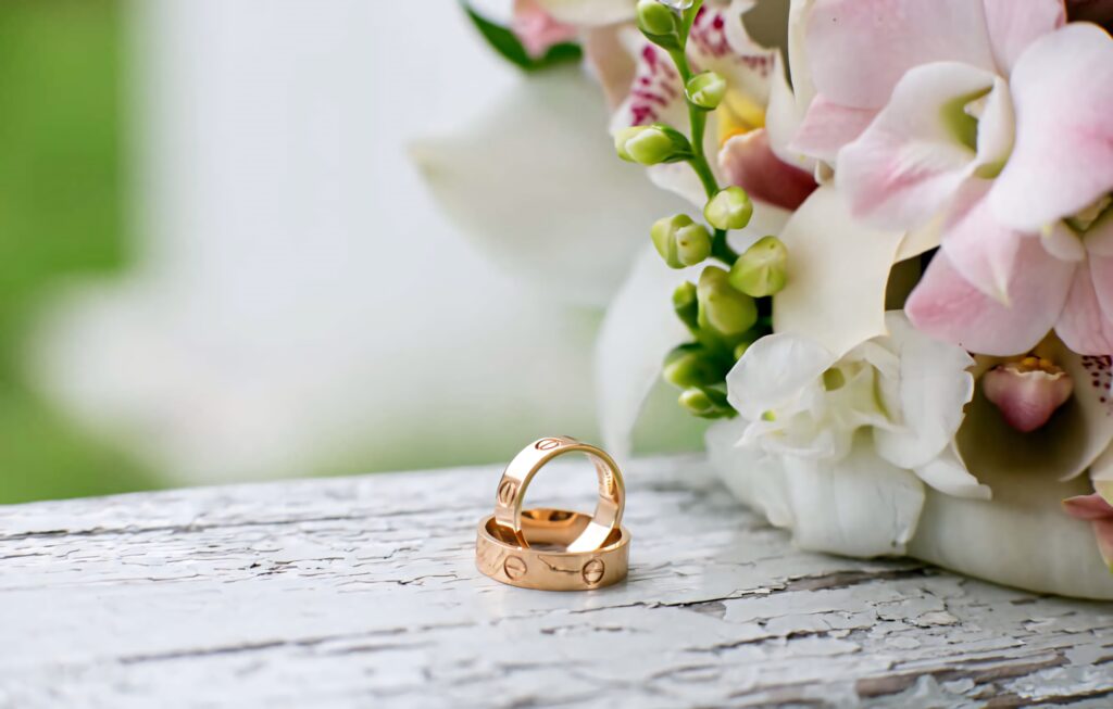 Pair of elegant gold engraved engagement rings on white wood with pastel pink floral background Wallpaper