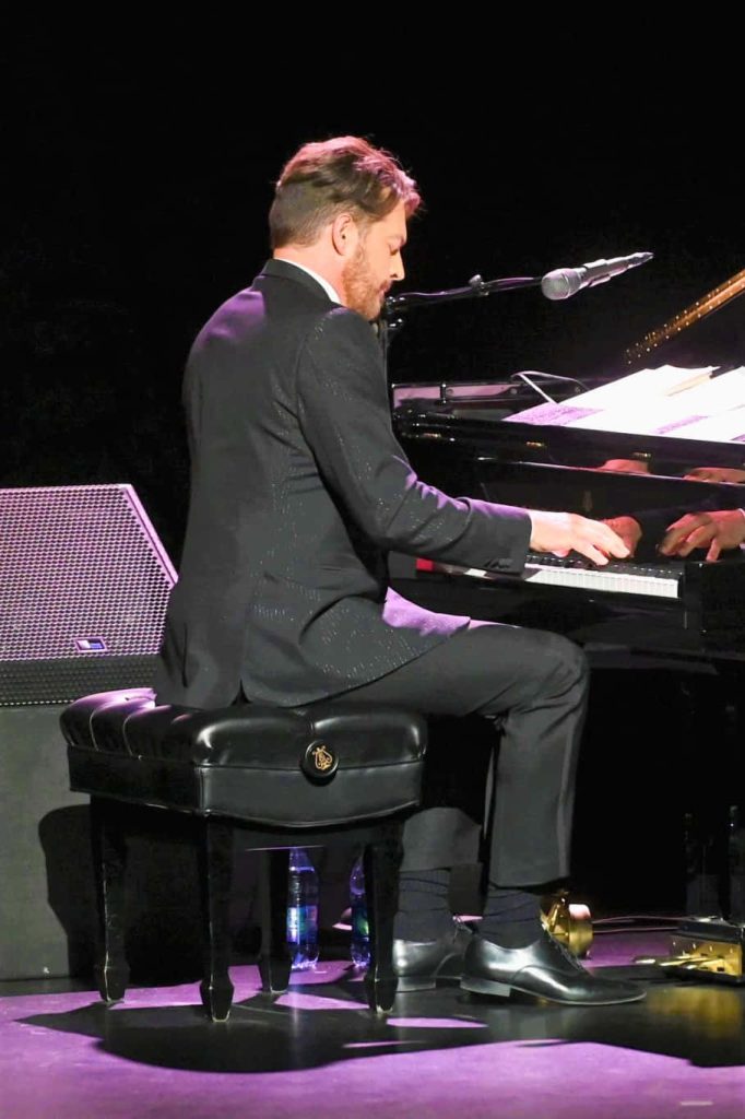 Harry Connick Jr. live performing jazz on grand piano in black suit with atmospheric lighting Wallpaper
