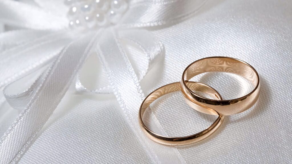 Two light gold engagement rings on white satin cushion with ribbon and pearls romantic elegance Wallpaper