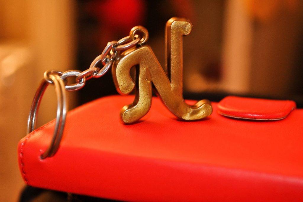 Close-up of metallic gold letter N keychain on vibrant red surface with soft bokeh background Wallpaper