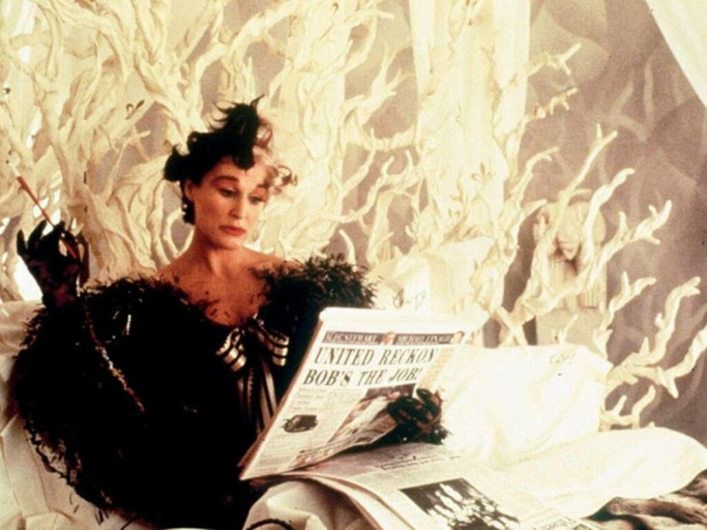 The Timeless Charm: Glenn Close Captivating as Cruella in Opulent Setting with Cigarette and Journals Wallpaper