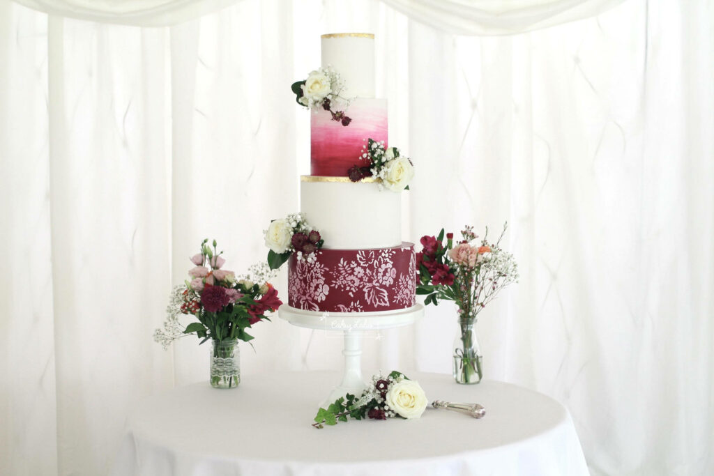 Elegant multi-layered wedding cake with scarlet gradient and floral decor on white pedestal Wallpaper