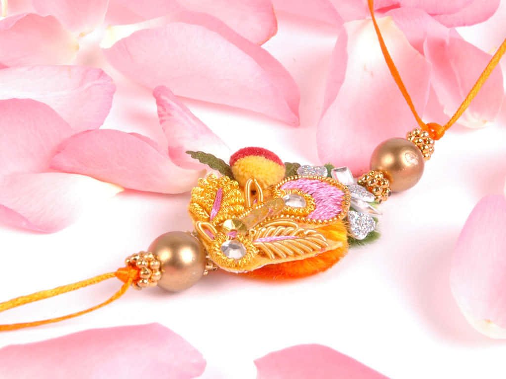 Ornate Rakhi with gold beads on pink flower petals Raksha Bandhan festival wallpaper background