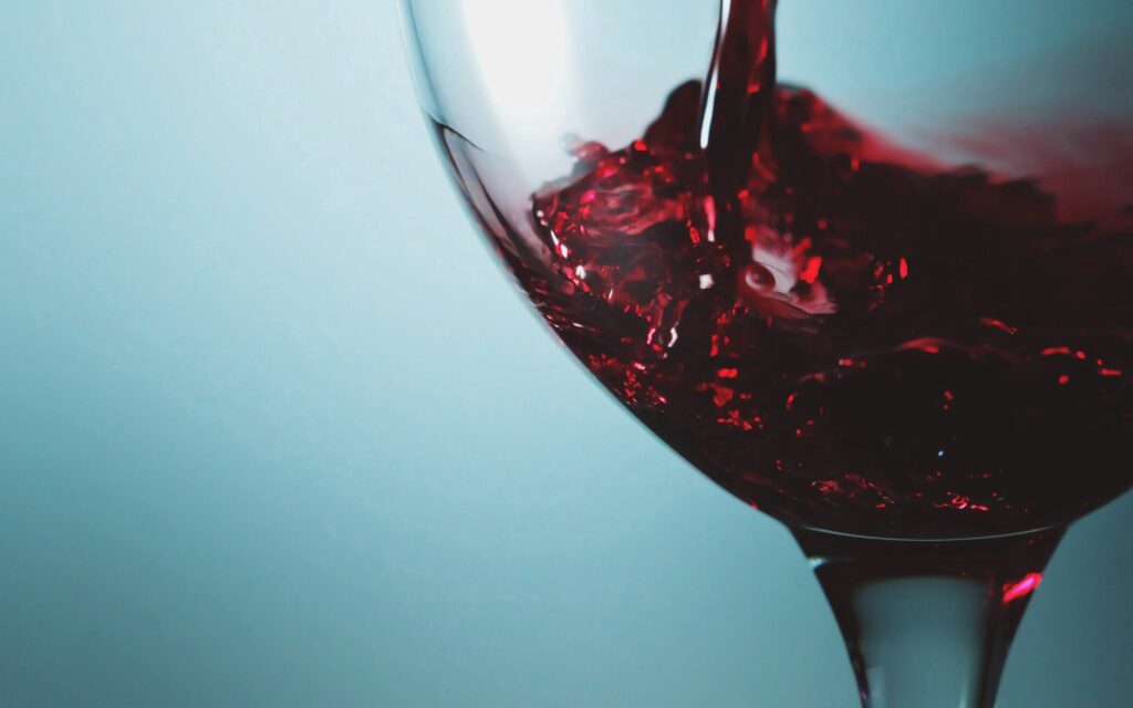 Fluid Elegance: Close-Up of Red Liquid Poured into Glass Wallpaper