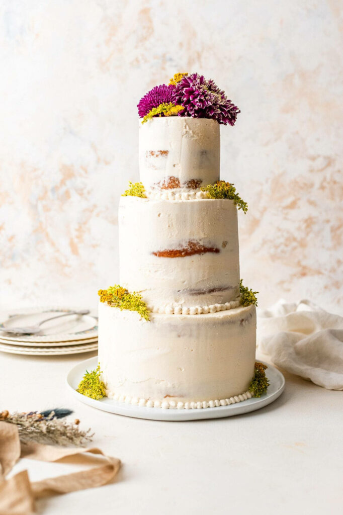 Three tiered rustic wedding cake with yellow purple chrysanthemums and greenery on creamy background Wallpaper