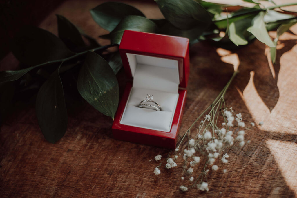Elegant silver engagement ring in red velvet box on rustic wood with natural light and greenery Wallpaper