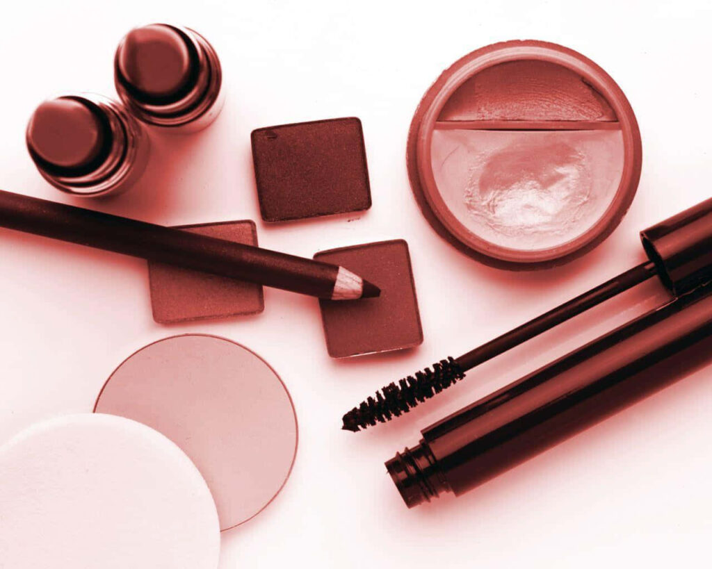Flat lay of makeup essentials in soft red tones with lipsticks eyeshadow brow pencil compact powder Wallpaper
