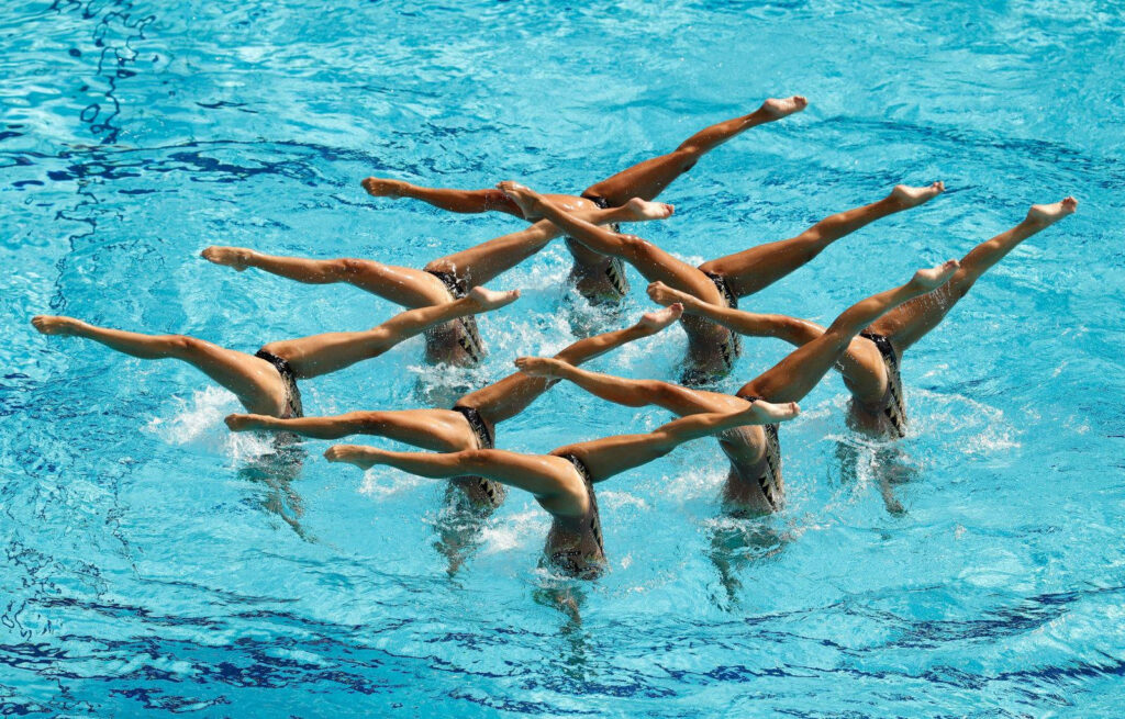 Synchronized swimmers gracefully performing a coordinated routine in crystal clear blue water wallpaper