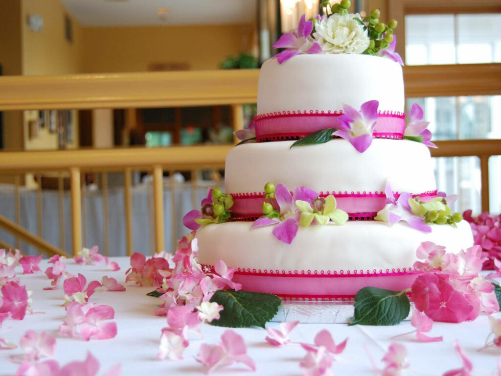 Elegant three-tiered white wedding cake with purple orchids roses and pink beaded ribbons wallpaper