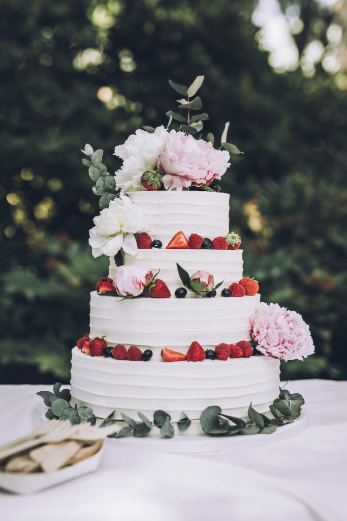 Elegant three-tiered wedding cake with mixed berries roses peonies on white textured frosting Wallpaper