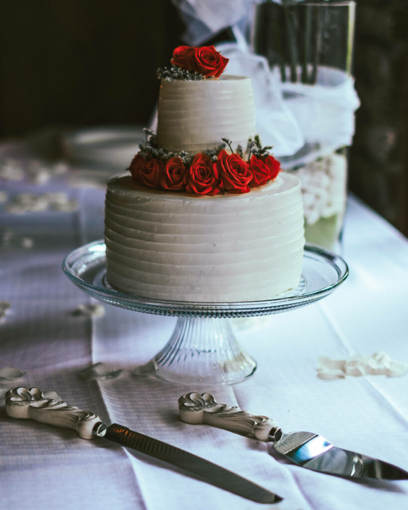 Elegant two-tiered wedding cake with red roses on glass stand against romantic floral background Wallpaper