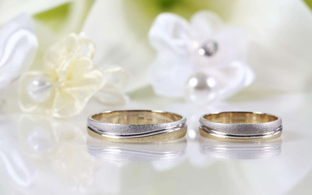 Elegant Silver Wedding Rings on Reflective Surface with White Flowers Wallpaper