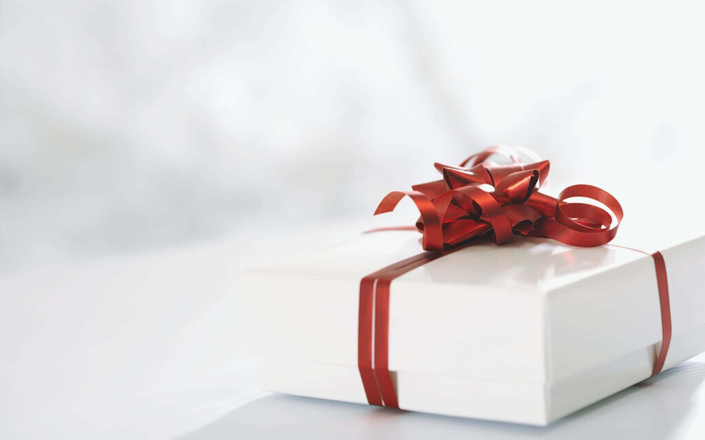 White gift box with shiny red ribbon on festive wallpaper background ready to surprise