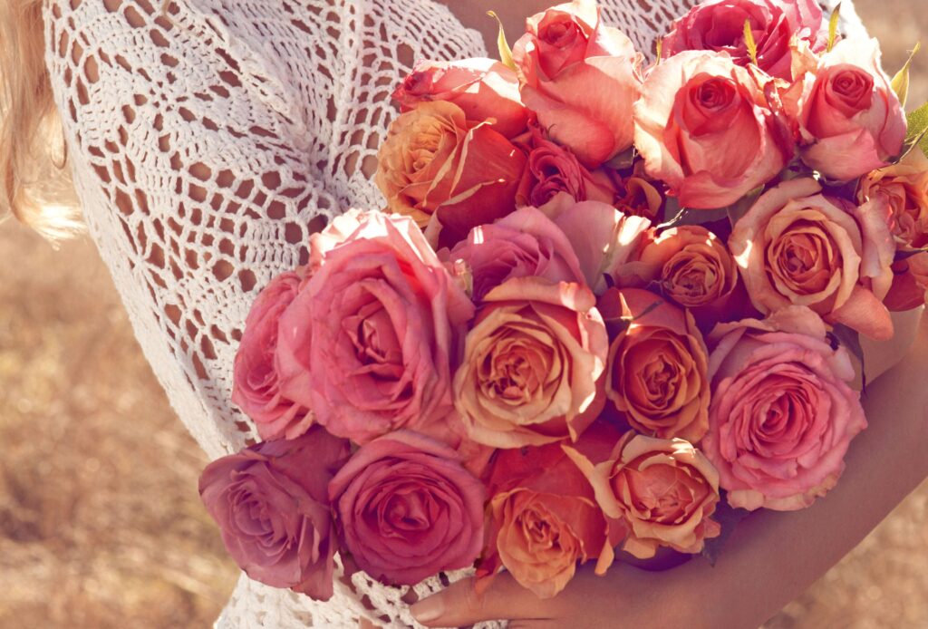Elegant Woman Holds Pink Peach Roses Against Earthy Background Wallpaper