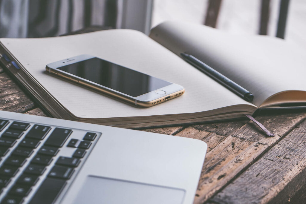 Modern Workspace: White Phone & Laptop on Rustic Wooden Desk Wallpaper