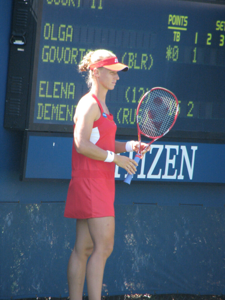 Elena Dementieva in red dress focused on tennis court with scoreboard backdrop in dynamic colors Wallpaper