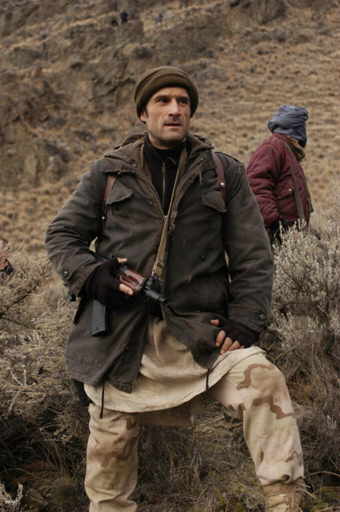 Elias Koteas in layered military clothing standing in rugged mountainous terrain with dramatic lighting Wallpaper