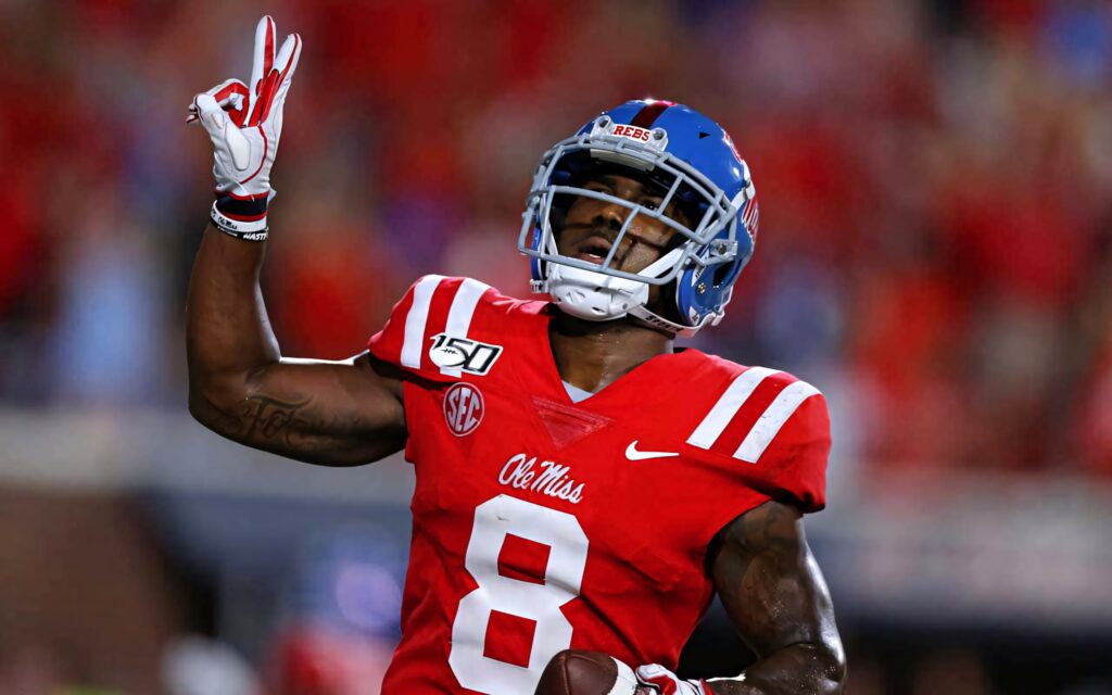 Elijah Moore in Ole Miss Football red and blue uniform making dynamic play under stadium lights Wallpaper
