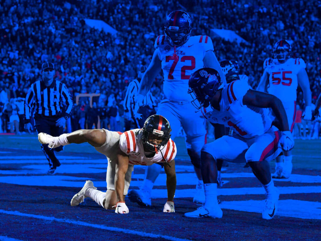 Elijah Moore celebrates touchdown with Ole Miss teammates on football field blue background wallpaper