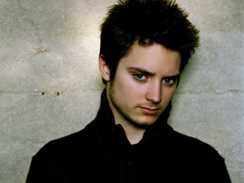 Elijah Wood close-up portrait with striking blue eyes against textured concrete wall background Wallpaper