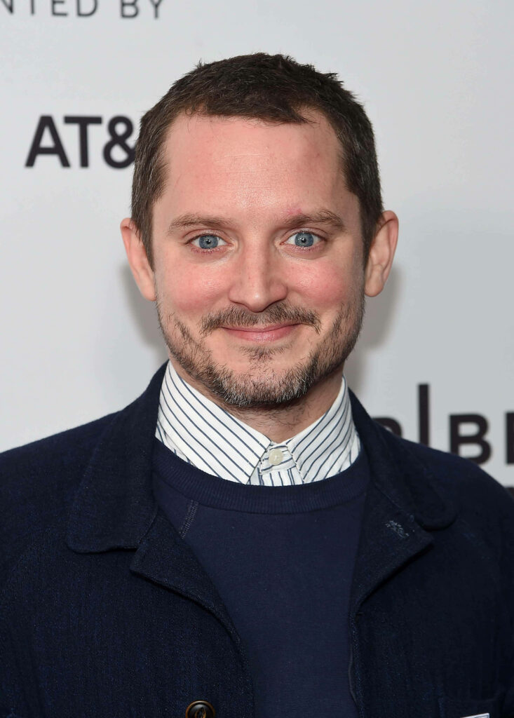 Elijah Wood wearing navy jacket and sweater smiling in clean background formal portrait wallpaper