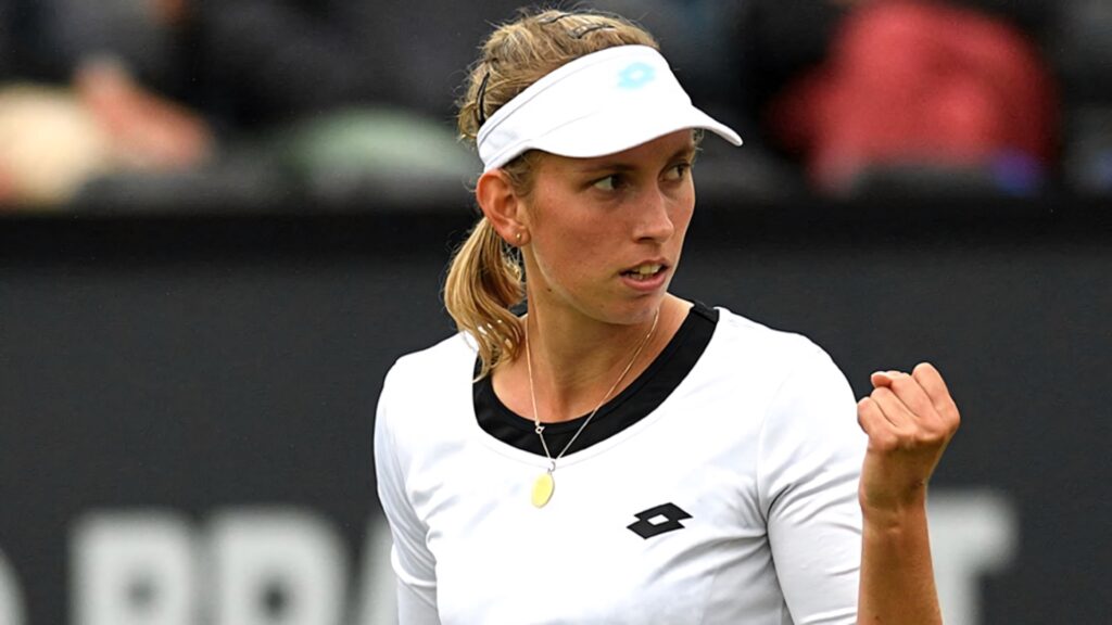 Elise Mertens celebrates with fist pump in white tennis outfit against dark background wallpaper